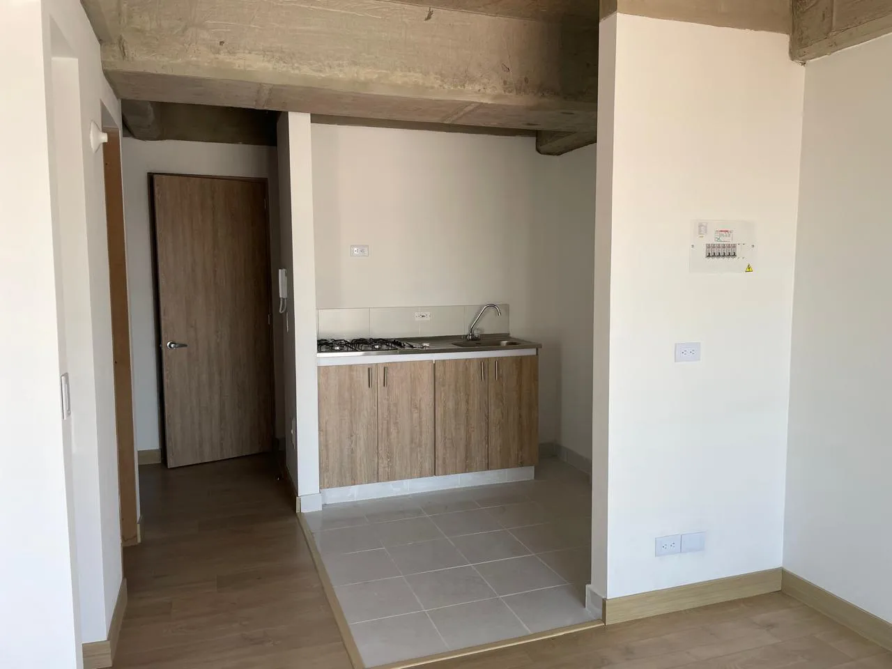 Cocina abierta con mueble bajo en madera, estufa de gas y lavaplatos, junto a la puerta de entrada.