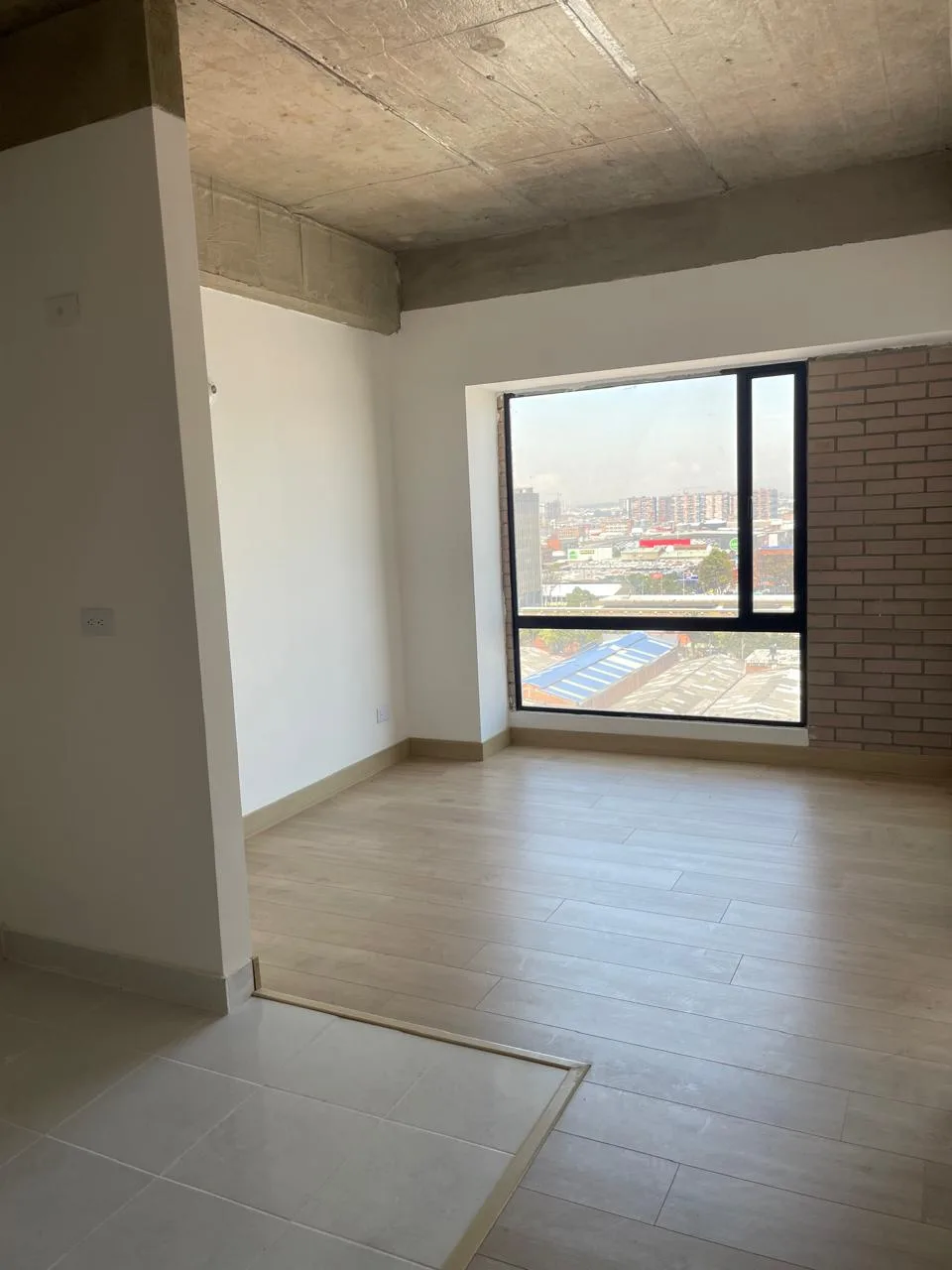 Habitación del apartamento con ventanal de piso a techo y vista despejada sobre la ciudad.