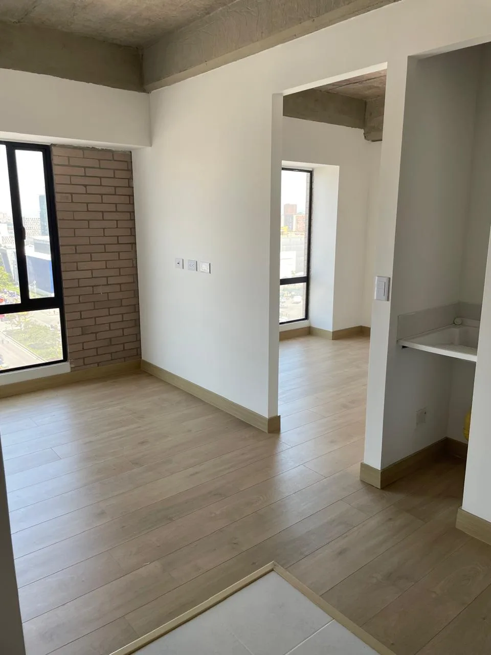 Sala-comedor del apartamento con muro de ladrillo a la vista, ventanal y zona de ropas al costado.