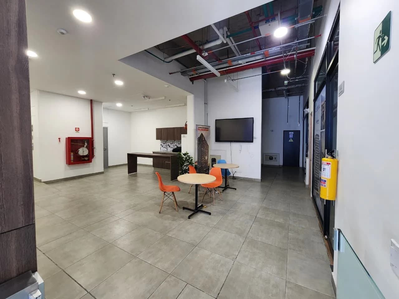 Zona de coworking del edificio, con mesas de trabajo, sillas y pantalla.