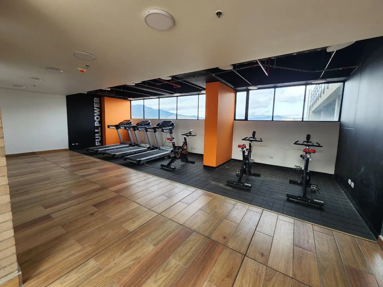 Gimnasio del edificio con caminadoras y bicicletas estáticas frente a un ventanal panorámico.