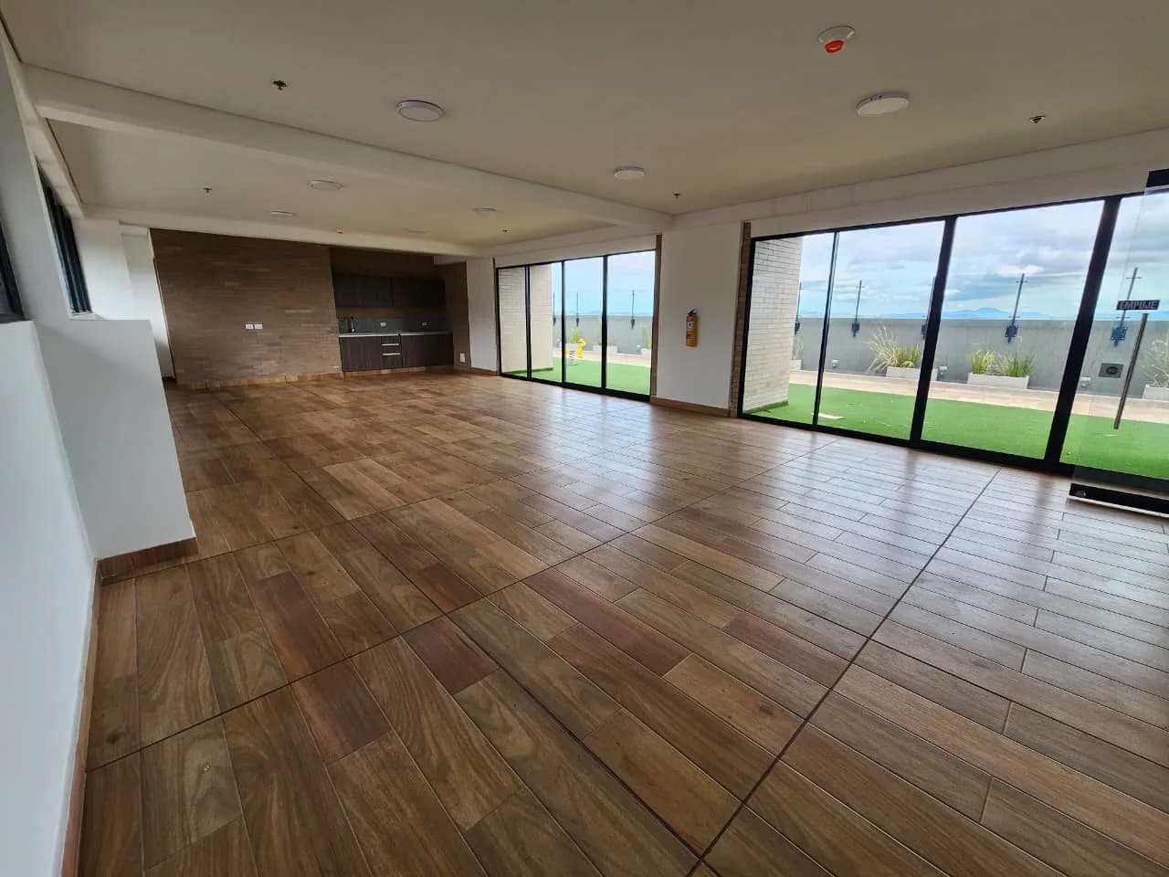 Salón social con piso de madera, barra al fondo y ventanales que dan a la terraza.