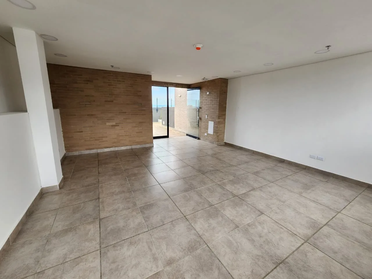 Salón de la azotea con muro de ladrillo y puerta de vidrio hacia la terraza.
