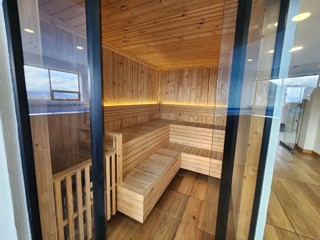 Sauna del edificio, revestido en madera, visto desde el exterior a través de su puerta de vidrio.
