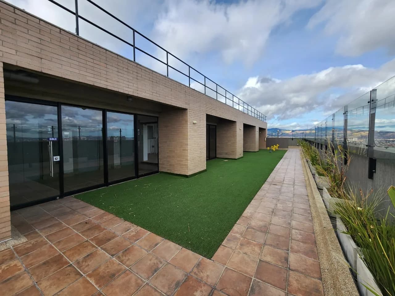 Terraza en la azotea de Astoria 19, con zona de grama, baranda de vidrio y los cerros de Bogotá al fondo.